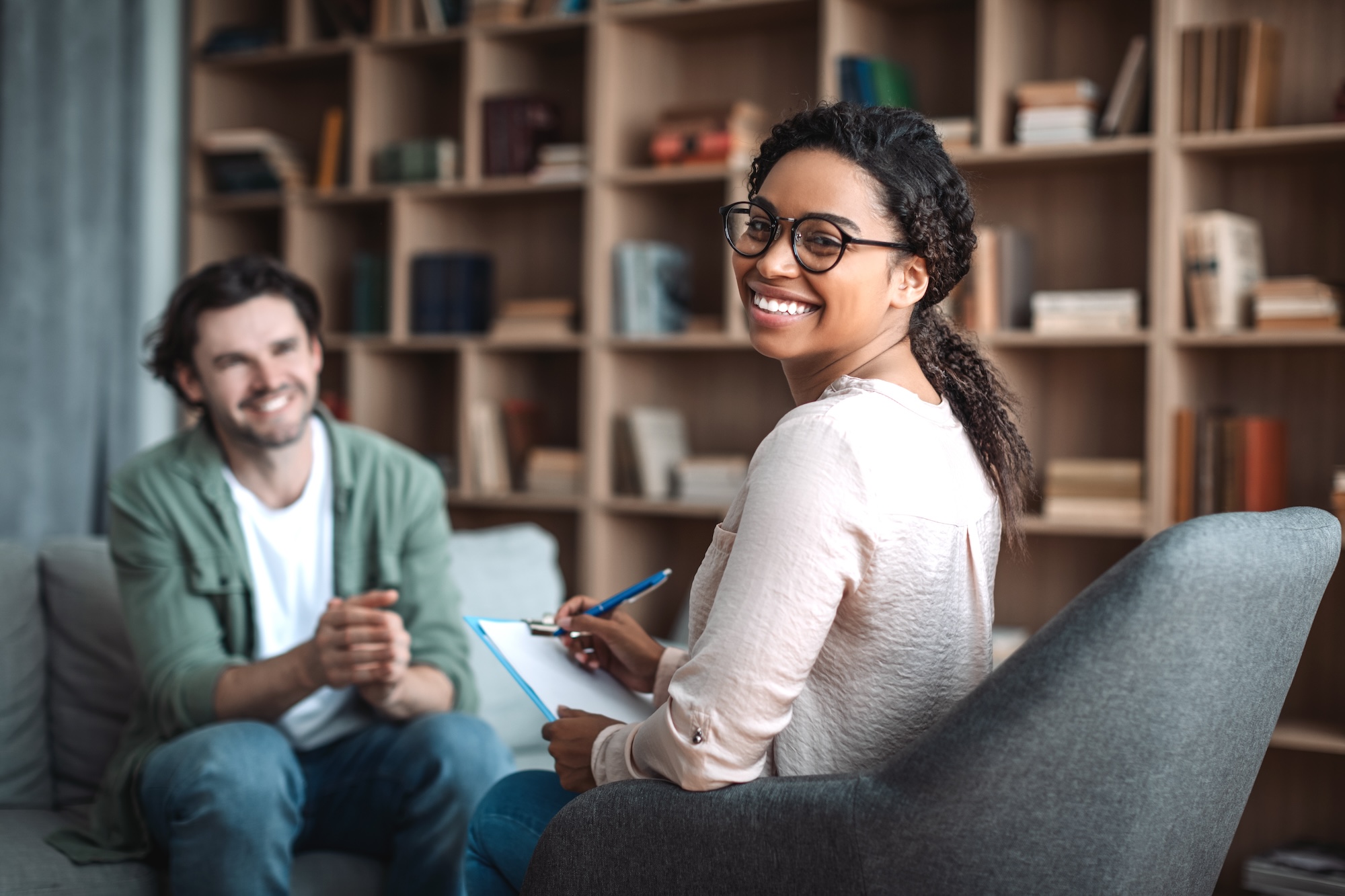 Man and female physician smiling holding clipboard, sitting in chairs